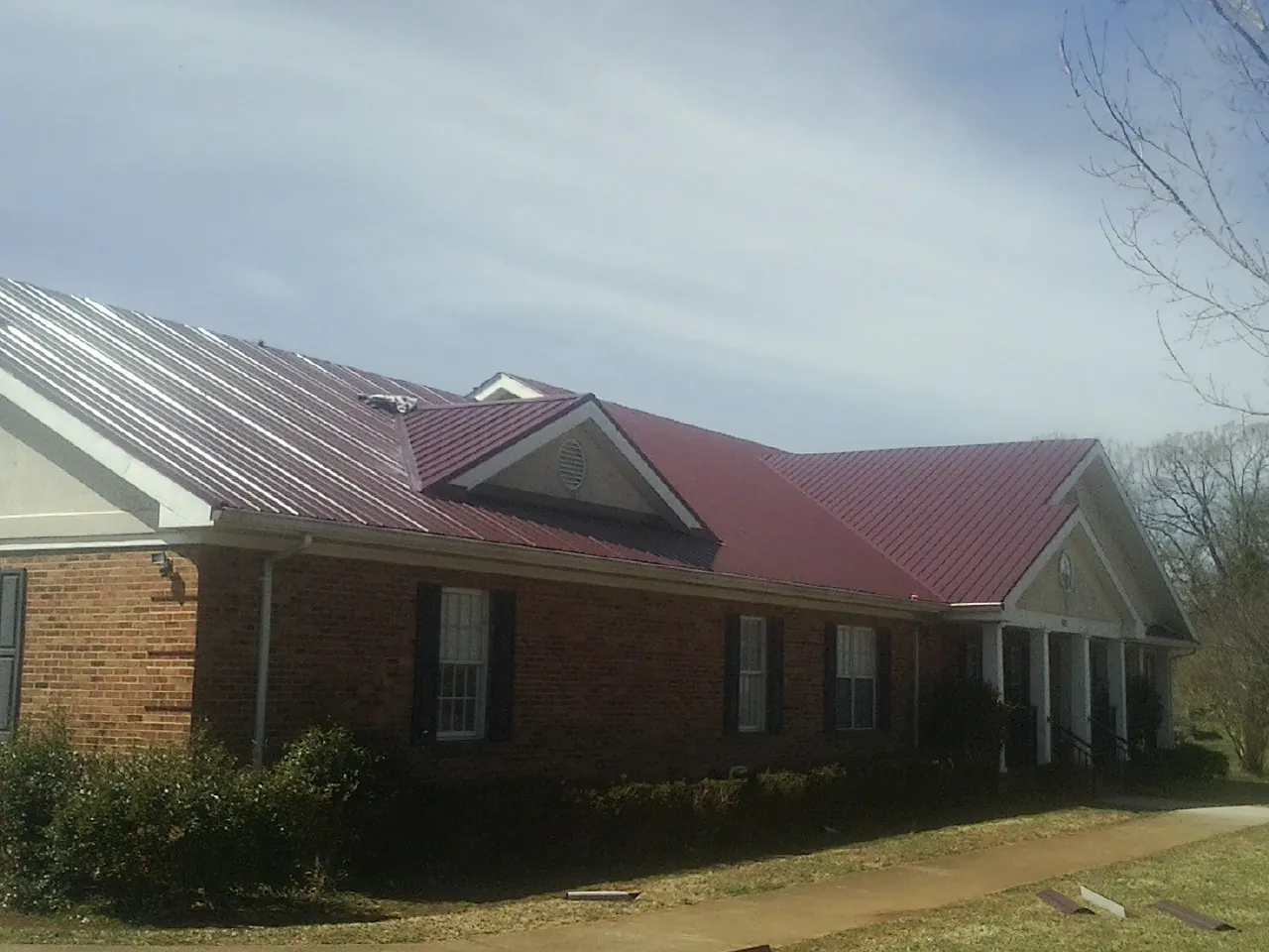 Red metal roof with gabled entries on a long brick building, from a Hail Damage Roof Repair job in Hilton Head Island