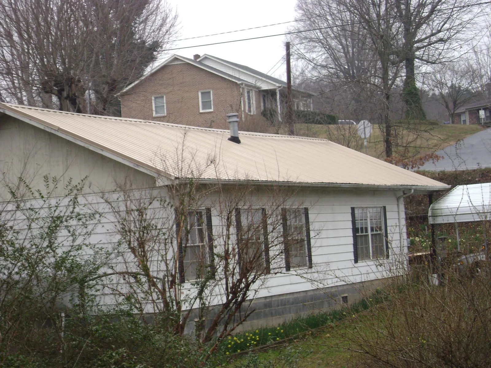 Tan metal roof on a white sided house set into a hillside — Commercial Roofing by Roofing Brothers in Hilton Head Island